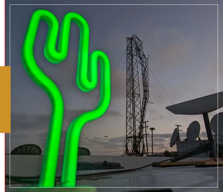 A neon cactus is lit up in front of an industrial building.